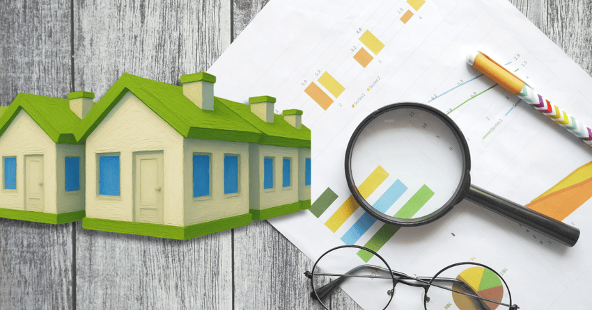 Home models, paper, pen, glasses, and a magnifying glass on a table.