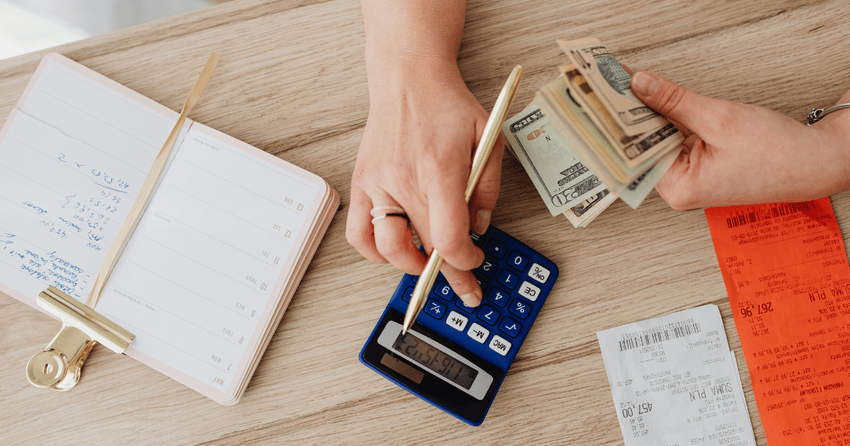 A person calculating household bills with cash, receipts, and a calculator, illustrating the cost of living in Cape Girardeau and everyday utility and living expenses.